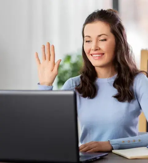 A young woman smiling and waving at her laptop screen at the start of a call