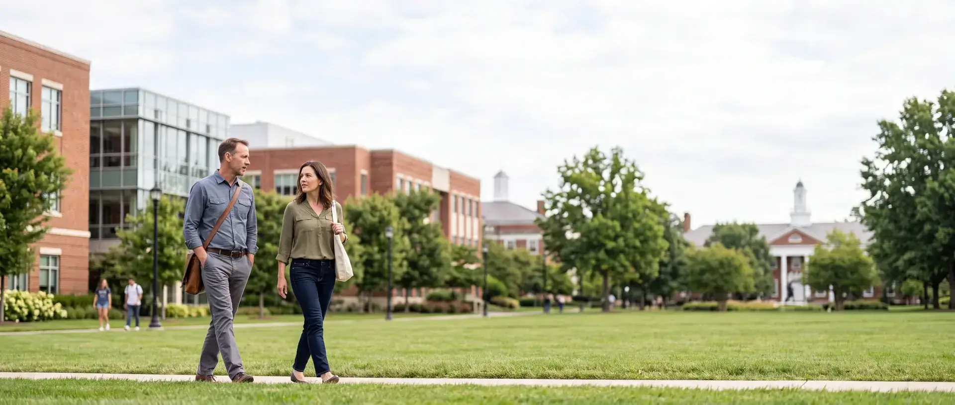 Two professionals walking and talking across a university quad