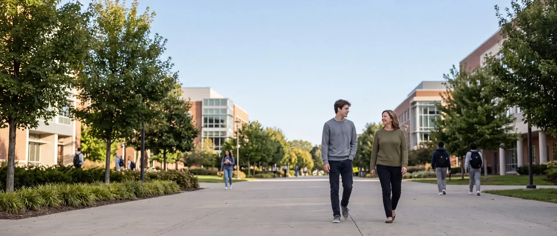A mother and her college-age son walking together and talking on a tree-lined campus walkway